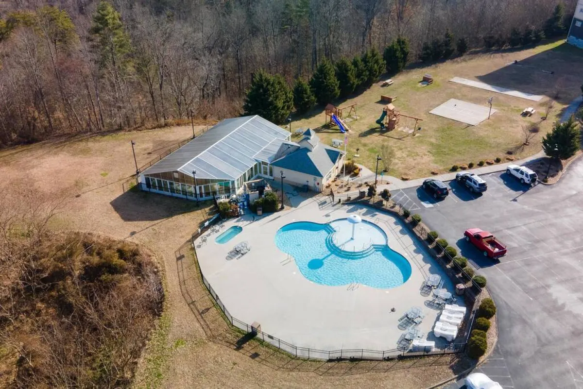 A joyful exterior scene centered around a large swimming pool, adjacent play area, and a recreational building, with families and children engaged in swimming and outdoor play. The mood is lively and communal, ideal for both active and relaxing moments.