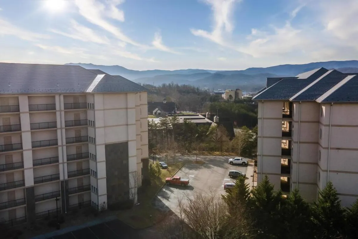 A tranquil view between resort buildings, showing ample parking, wide paths, and mountains in the background. The layout emphasizes convenient movement throughout the area and easy access to nearby attractions, with open sight lines and walkable paths.