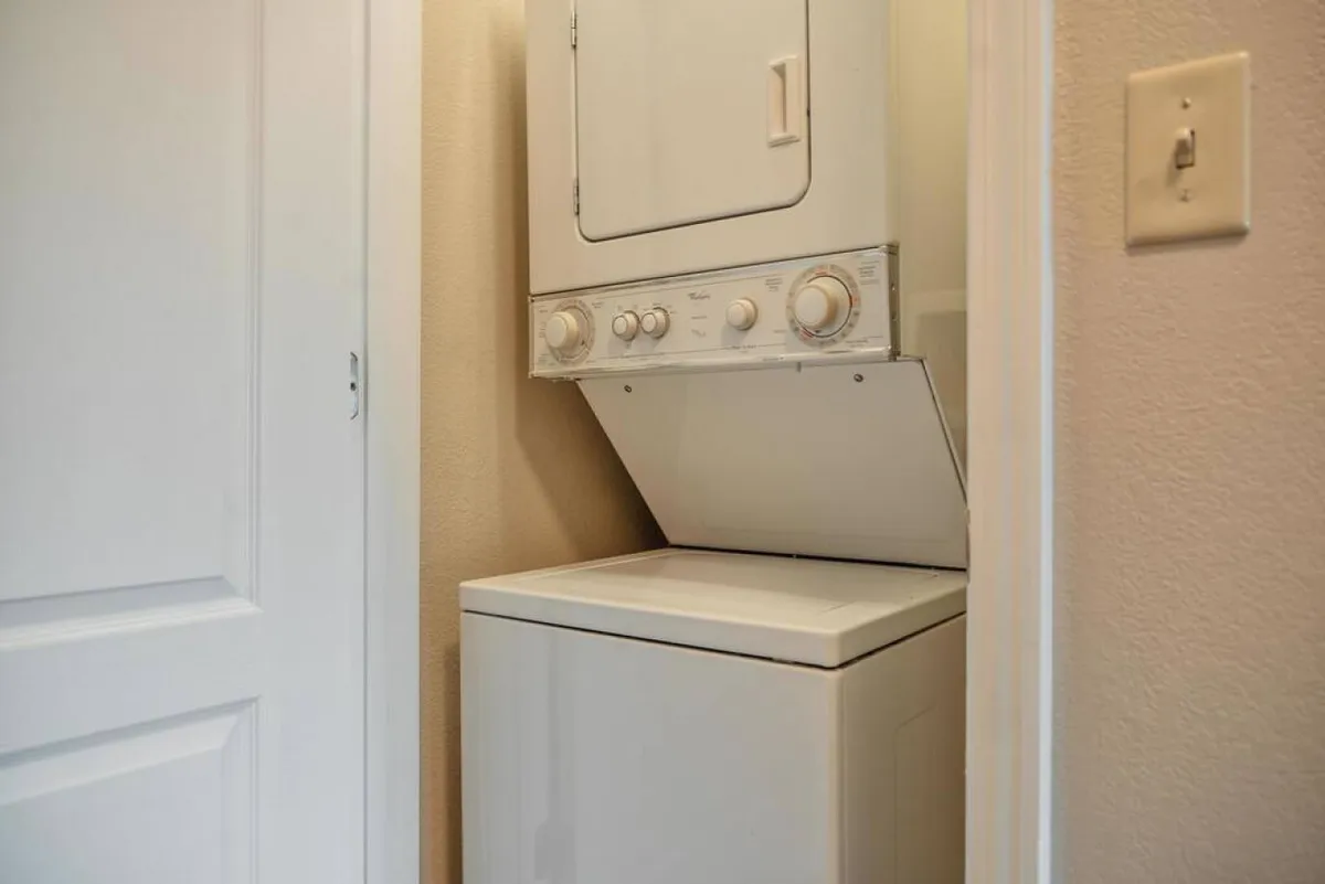 A practical laundry area with a stacked washer and dryer unit, a white door, and a textured wall. The space is clean and organized, ready for use.