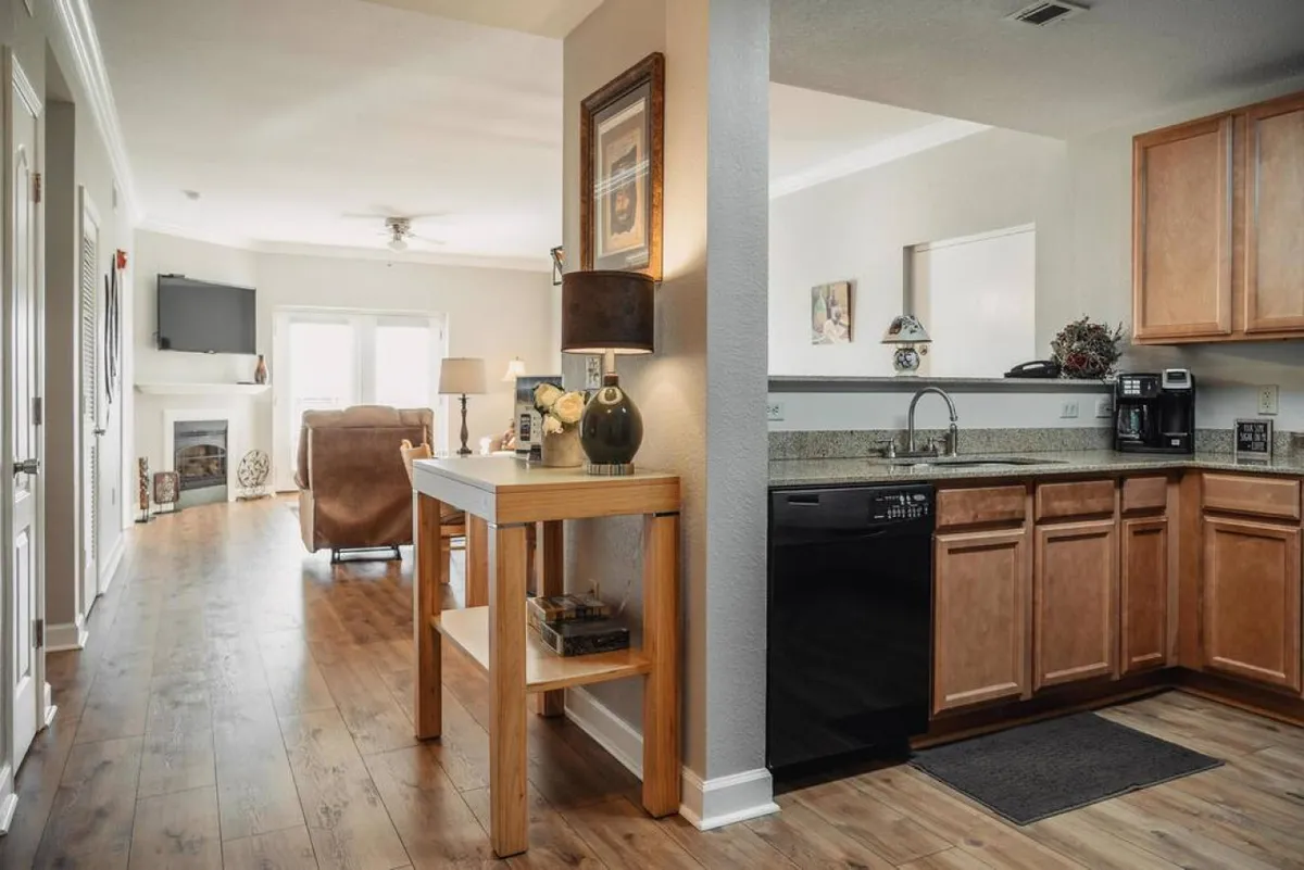 An inviting, open living space that seamlessly connects a modern kitchen, a dining table, and a comfortable lounge area. The decorative lamp and pops of color create a festive atmosphere ideal for celebrations, casual meals, and group relaxation.