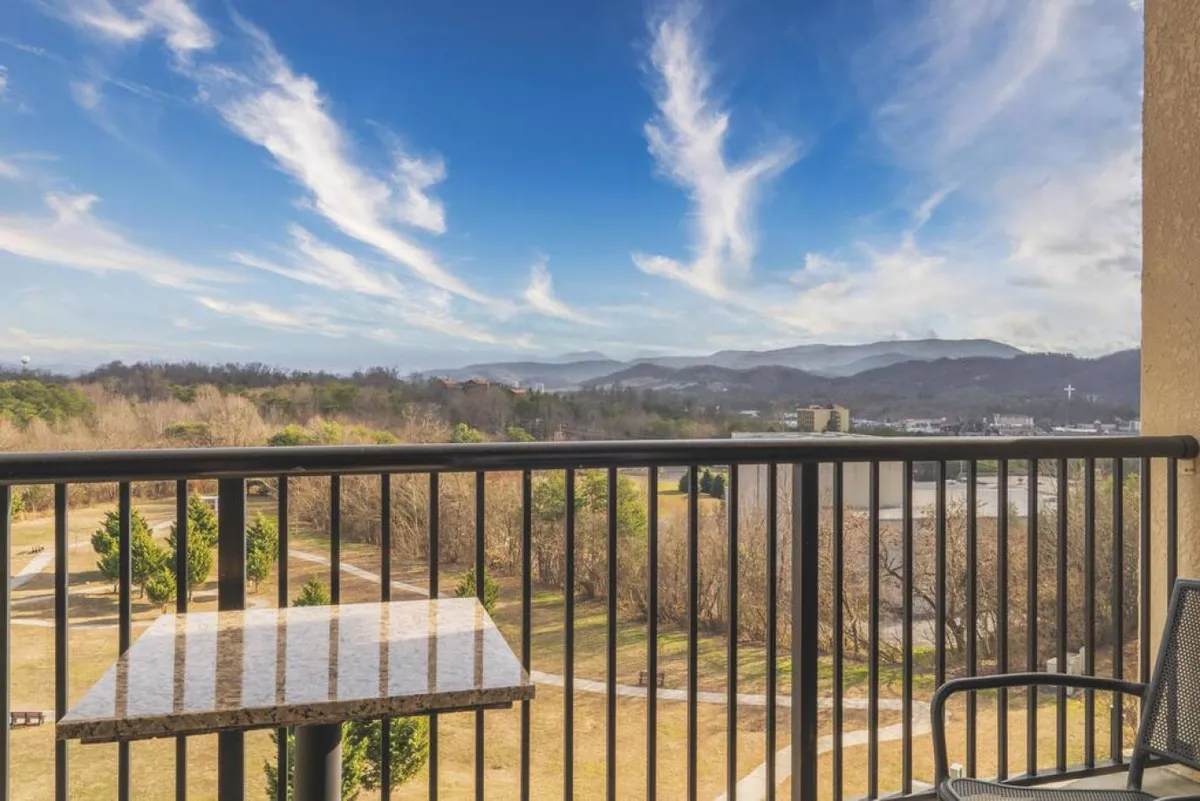 A peaceful balcony scene overlooking a stunning mountain range, with comfortable outdoor furniture set for relaxation. The sky is alive with the promise of sunset or fireworks, inviting guests to unwind while soaking up breathtaking views.