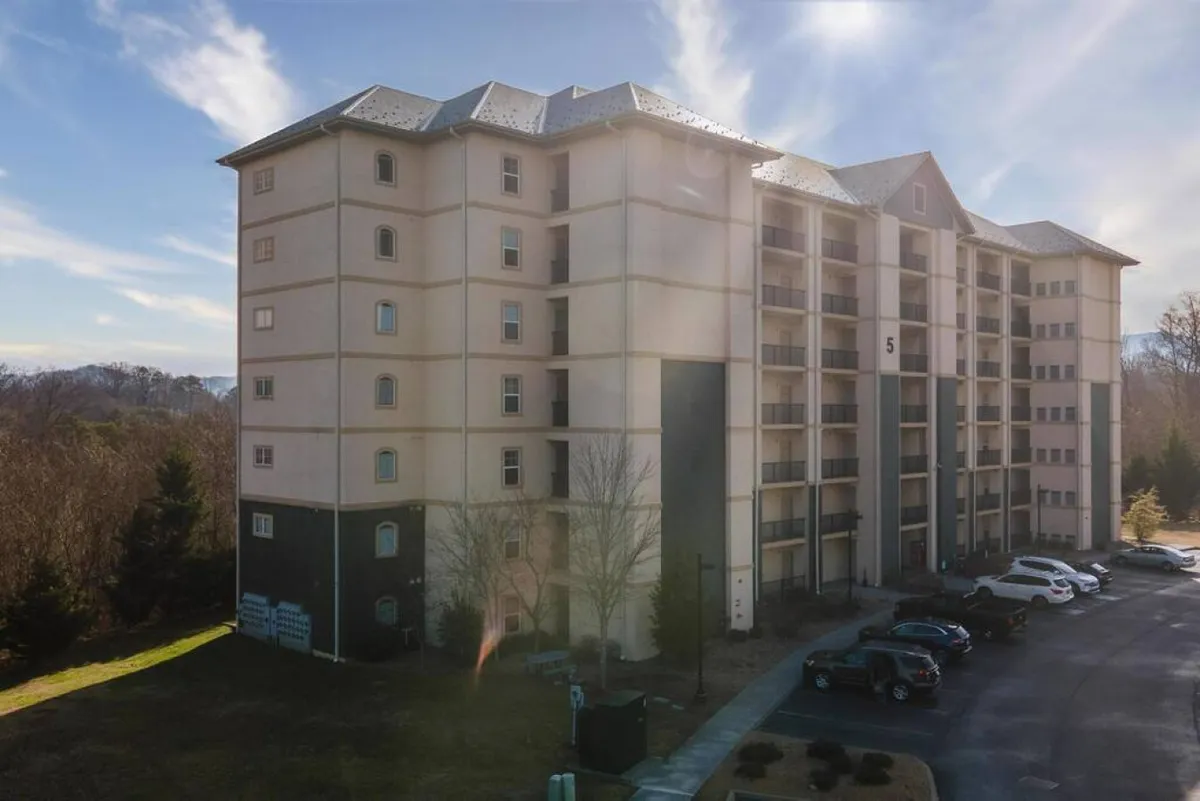 A modern four-story building with several private balconies overlooking landscaped grounds, perfect for social gatherings or relaxing after a night out. The sunset light enhances the inviting atmosphere, hinting at views of the surrounding area.