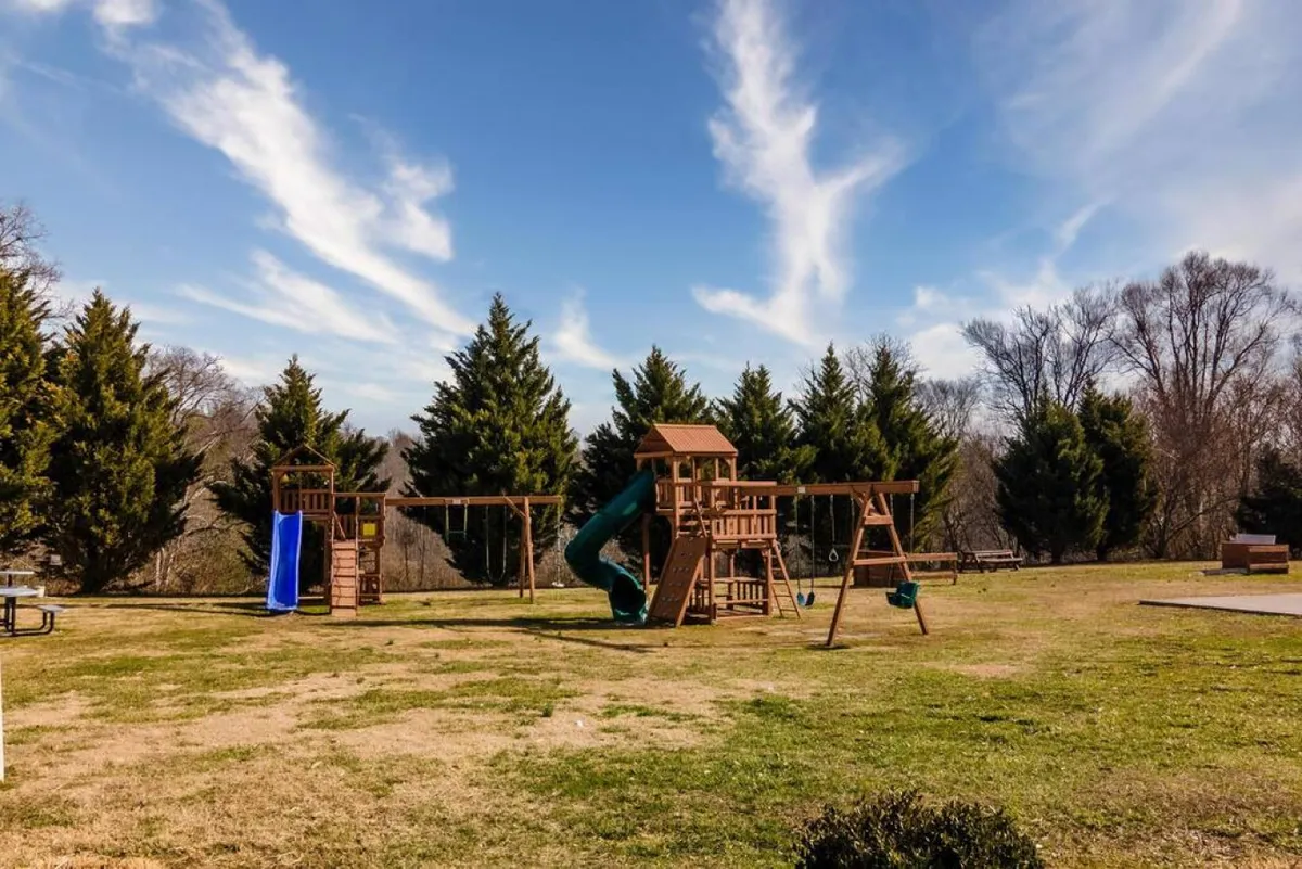 A colorful playground with swings and a slide sits in a sunny green area, ready for children and families to enjoy. The scene radiates playfulness and joy, with ample space for kids to explore and gather for group activities.