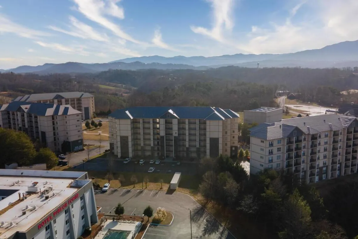 A tranquil exterior scene featuring a mountain range in the background, rows of resort buildings, and a parking lot in the foreground. The peaceful setting suggests opportunities for outdoor activities, relaxation, and exploration.